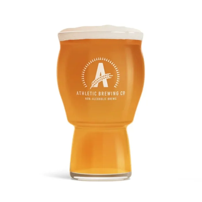 Glass of golden non-alcoholic beer by Athletic Brewing Co., featuring frothy head and signature branding, perfect for a refreshing experience.