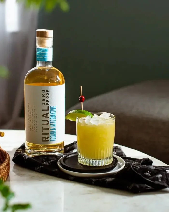 Ritual Zero Proof tequila alternative with a garnished cocktail on a table.