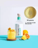 Ritual Zero Proof bottle with citrus cocktail, fresh fruit, and 90-point Beverage Testing Institute award.