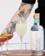Ritual Zero Proof bottle with elegant cocktails, including a lavender garnish, in a vibrant setting.