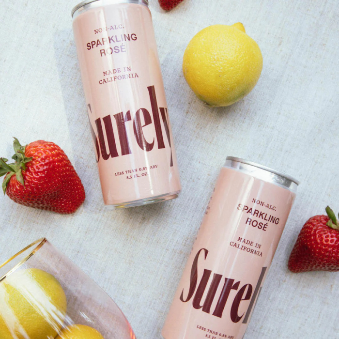 Surely non-alcoholic sparkling rosé cans with fresh strawberries and lemons on a light background.