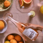 Hand holding Surely rosé wine bottle with citrus fruits, creating a fresh and vibrant setup.