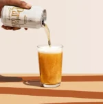 Golden beverage being poured from a branded can into a glass, showcasing refreshing drink texture.