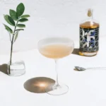 Elegant cocktail with Monday whiskey bottle on a minimalistic table setting.