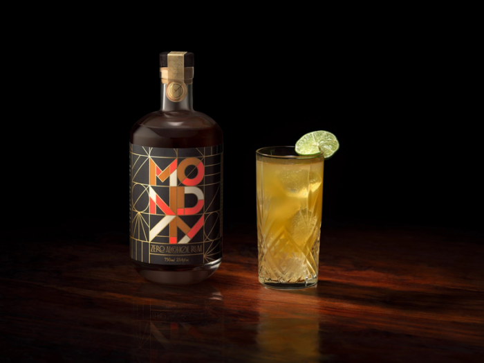 Monday Zero Alcohol Whiskey served alongside a tall iced cocktail garnished with a lime, on a dark wooden table.