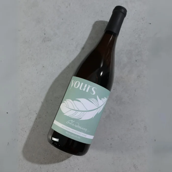 Bottle of Yours non-alcoholic wine laying on a minimalist concrete surface with soft lighting.