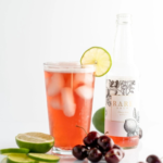 Rare Brew cherry drink with lime garnish, fresh cherries, and bottle in the background.