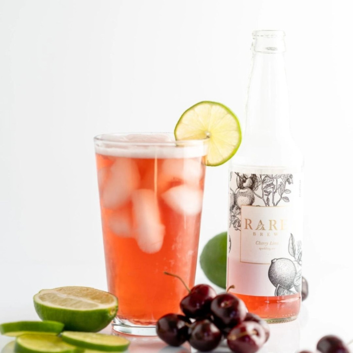 Rare Brew cherry drink with lime garnish, fresh cherries, and bottle in the background.
