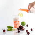 Rare Brew cherry drink poured into a glass with lime, cherries, and fresh limes on display.