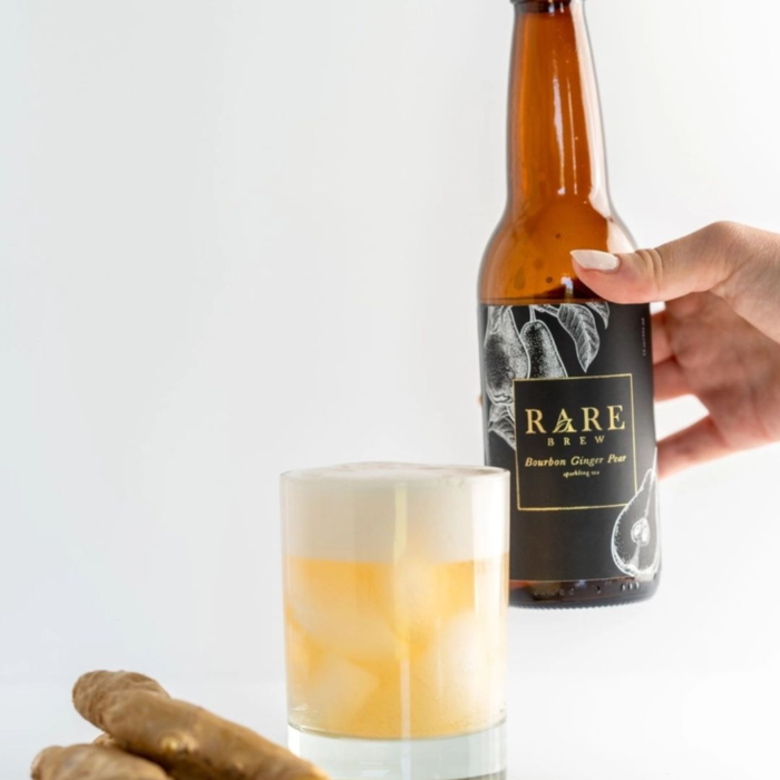 Rare Brew bottle with a creamy ginger mocktail, garnished and served alongside fresh ginger root.