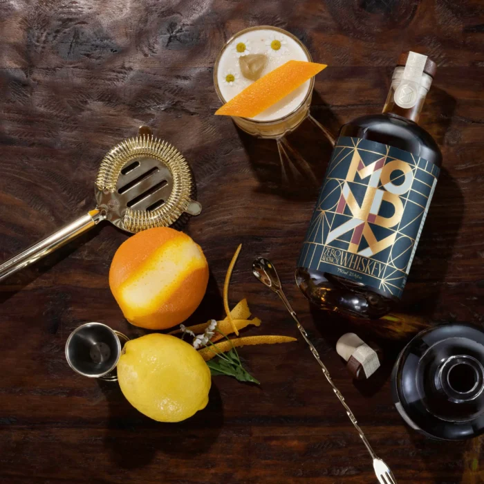 Monday Zero Alcohol Whiskey bottle with a crafted cocktail, citrus garnish, and bar tools on a wooden table.