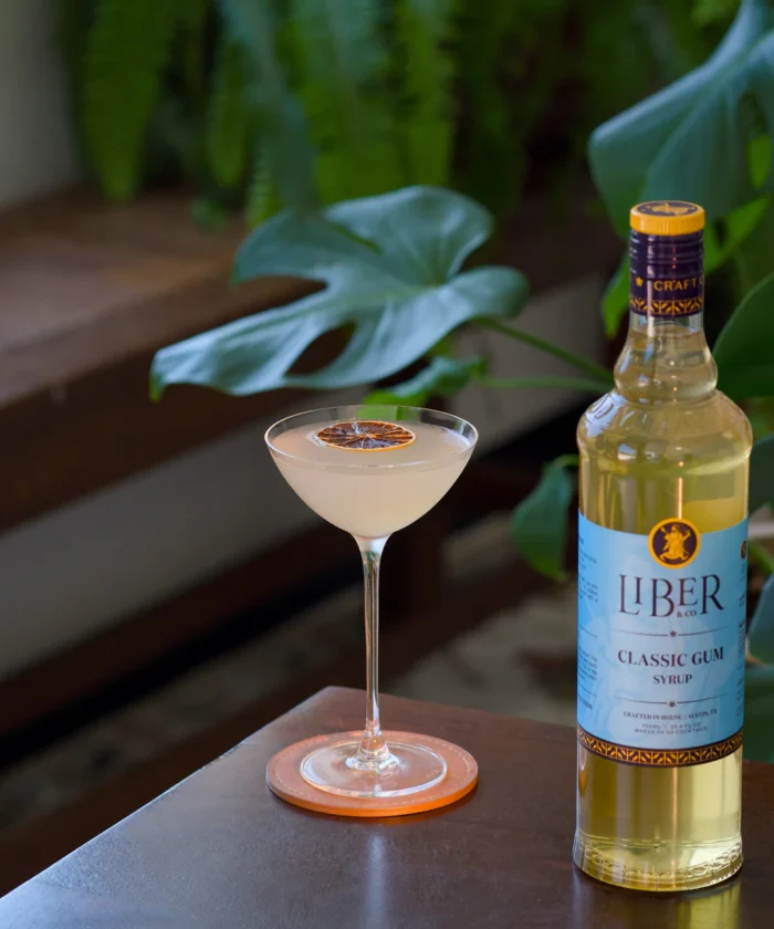 Liquor bottle beside a cocktail glass on a wooden surface with greenery in the background.