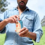 Man in denim shirt opening a can of non-alcoholic craft beer outdoors, showcasing a refreshing moment in a scenic setting.
