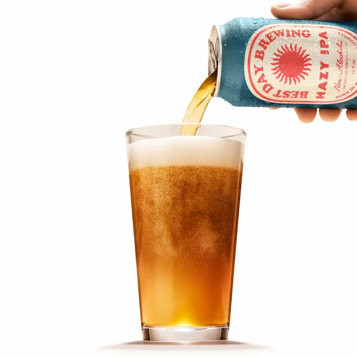 Pouring a golden non-alcoholic Hazy IPA into a glass, showcasing a frothy head and vibrant color for a refreshing craft beer experience.
