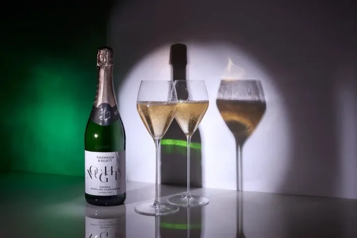 Sparkling wine bottle with two filled glasses and dramatic spotlight, perfect for celebrations.