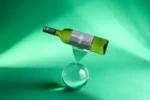 White wine bottle balanced on a glass sphere against a vibrant green background with artistic lighting.