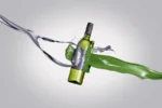 Creative depiction of a green wine bottle splashed with vibrant liquid and wrapped in metallic ribbon.
