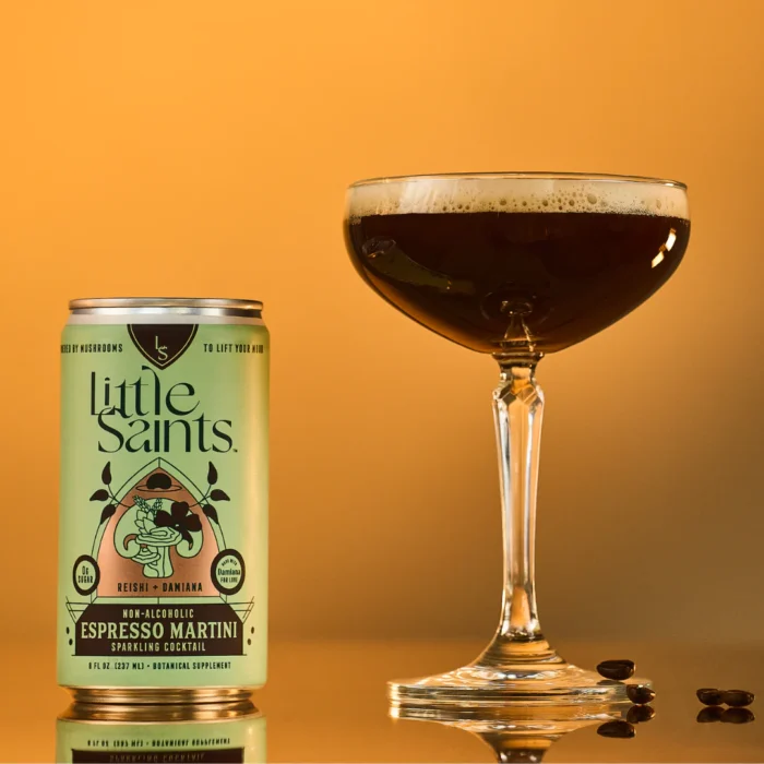Little Saints Espresso Martini can next to a dark, frothy cocktail in a coupe glass against orange background.