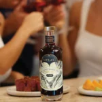 Melati Classic bottle on a table with fruit plates, surrounded by people toasting in the background.