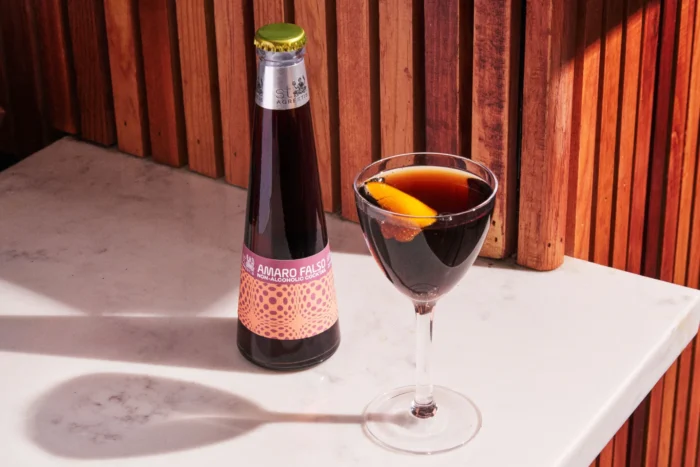 Amaro Falso non-alcoholic cocktail bottle with a dark, citrus-garnished cocktail in a glass on a marble surface.