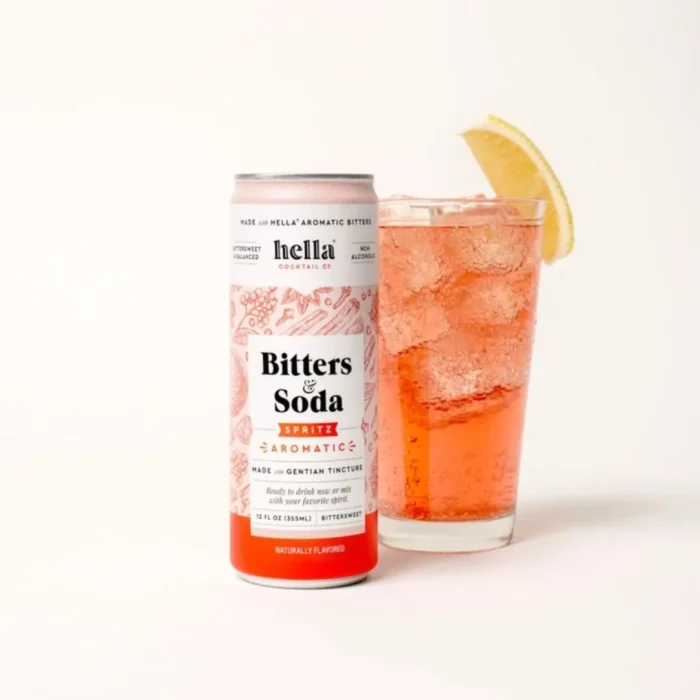 Hella Bitters & Soda can with a tall glass of red bitters beverage, garnished with a lemon wedge