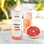 Hella Bitters & Soda can with a glass of sparkling grapefruit drink and sliced grapefruit on a table.