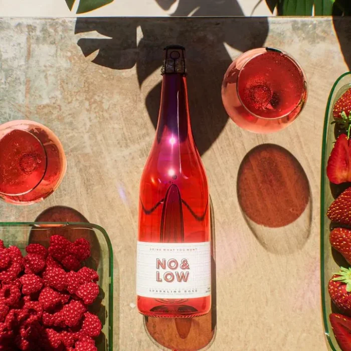 No & Low rosé wine bottle surrounded by fresh raspberries, strawberries, and glasses on a sunny table.