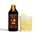 Curious Elixirs No. 2 bottle with a refreshing ginger-lime mocktail garnished with a lime slice.
