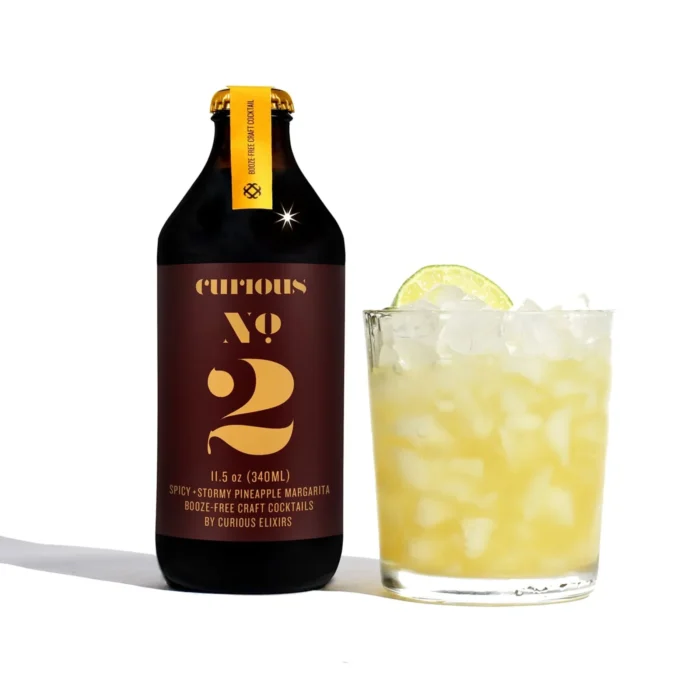 Curious Elixirs No. 2 bottle with a refreshing ginger-lime mocktail garnished with a lime slice.