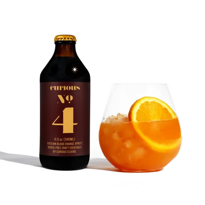 Curious Elixirs No. 4 bottle with a Sicilian blood orange spritz mocktail garnished with fresh orange slices.