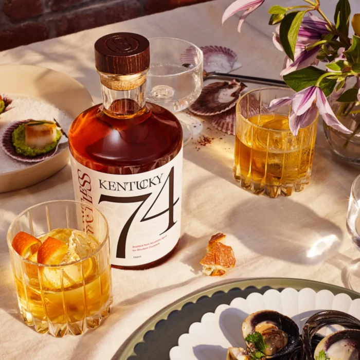Spiritless Kentucky 74 bottle on an elegant dining table with cocktails, seafood dishes, and vibrant floral decor, creating a sophisticated dining ambiance.