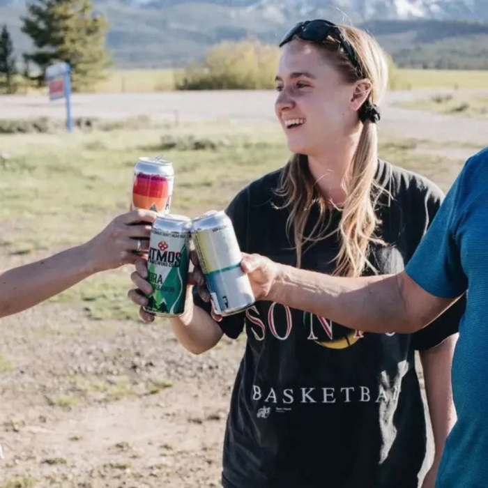 Group of friends enjoying a toast with Atmos Brewing Co. Kora NA Double Hop IPA and other non-alcoholic craft beers in a scenic outdoor setting.