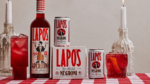 Lapo's Negroni drink cans, bottle, and packaging on a checkered table with a red cocktail glass.