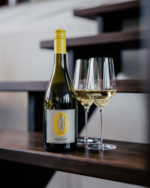 Bottle of white wine with two glasses placed on a wooden staircase in a modern, minimalist setting.