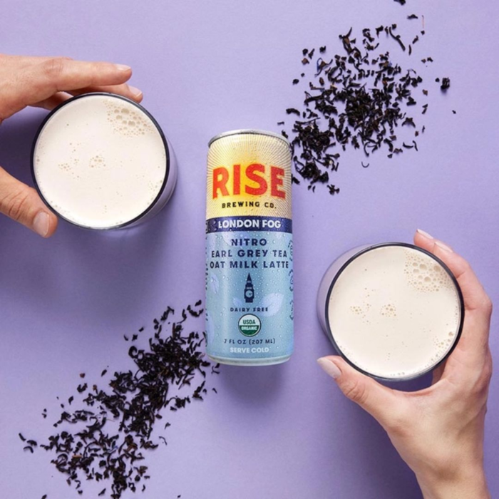 Rise Nitro London Fog Earl Grey Tea Oat Milk Latte can with two glasses and loose tea leaves on a lavender background.