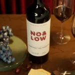 Close-up of No & Low alcohol-removed Cabernet Sauvignon with a glass, grapes, and cheese on a wooden table.