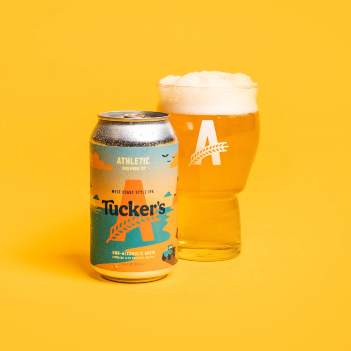 Can of Athletic Brewing Co.'s Tucker's West Coast Style IPA alongside a glass of golden, frothy non-alcoholic beer, set against a vibrant yellow background.