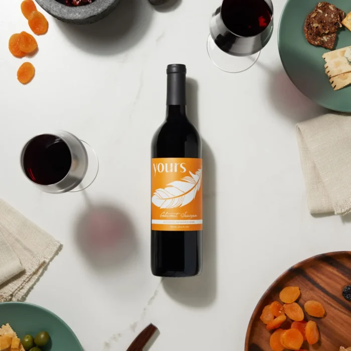 Flat lay of a wine bottle surrounded by glasses, dried fruits, olives, and cheese on a white table.