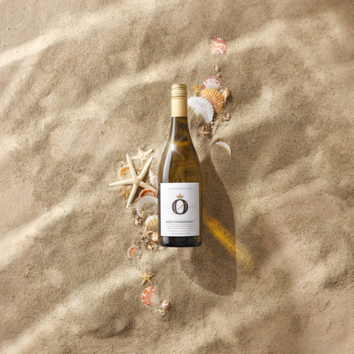 Bottle of white wine elegantly displayed on sandy terrain surrounded by seashells and starfish.