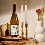 Bottle of Sovi Chenin Blanc displayed with cheese, nuts, candles, and rustic decor for a cozy ambiance.