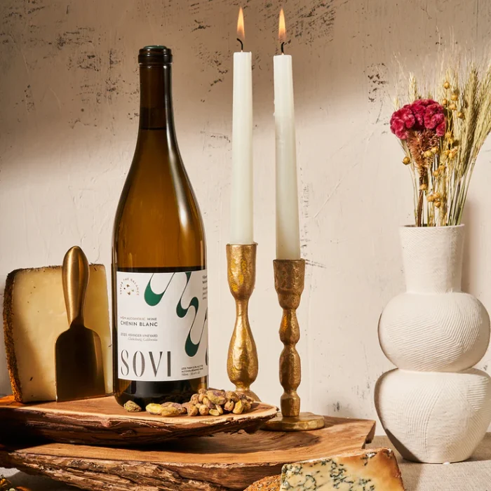 Bottle of Sovi Chenin Blanc displayed with cheese, nuts, candles, and rustic decor for a cozy ambiance.