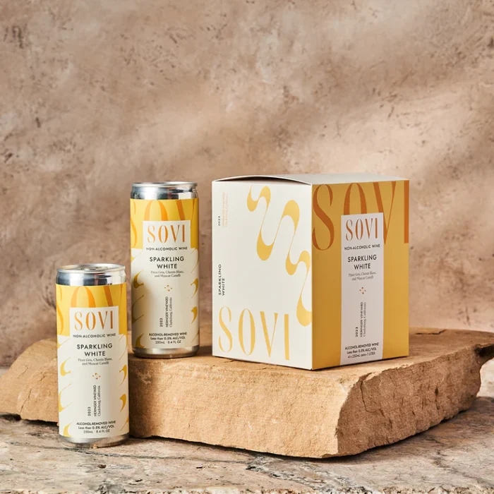 Sovi Sparkling White non-alcoholic wine cans and box on a rustic stone surface with elegant design.