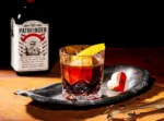 The Pathfinder non-alcoholic spirit bottle with a dark cocktail garnished with orange peel on a rustic tray.