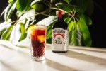 The Pathfinder non-alcoholic spirit bottle with an iced cocktail garnished with citrus, set against leafy greenery.