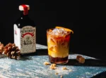 The Pathfinder non-alcoholic spirit bottle with a layered cocktail garnished with orange peel on a rustic surface.