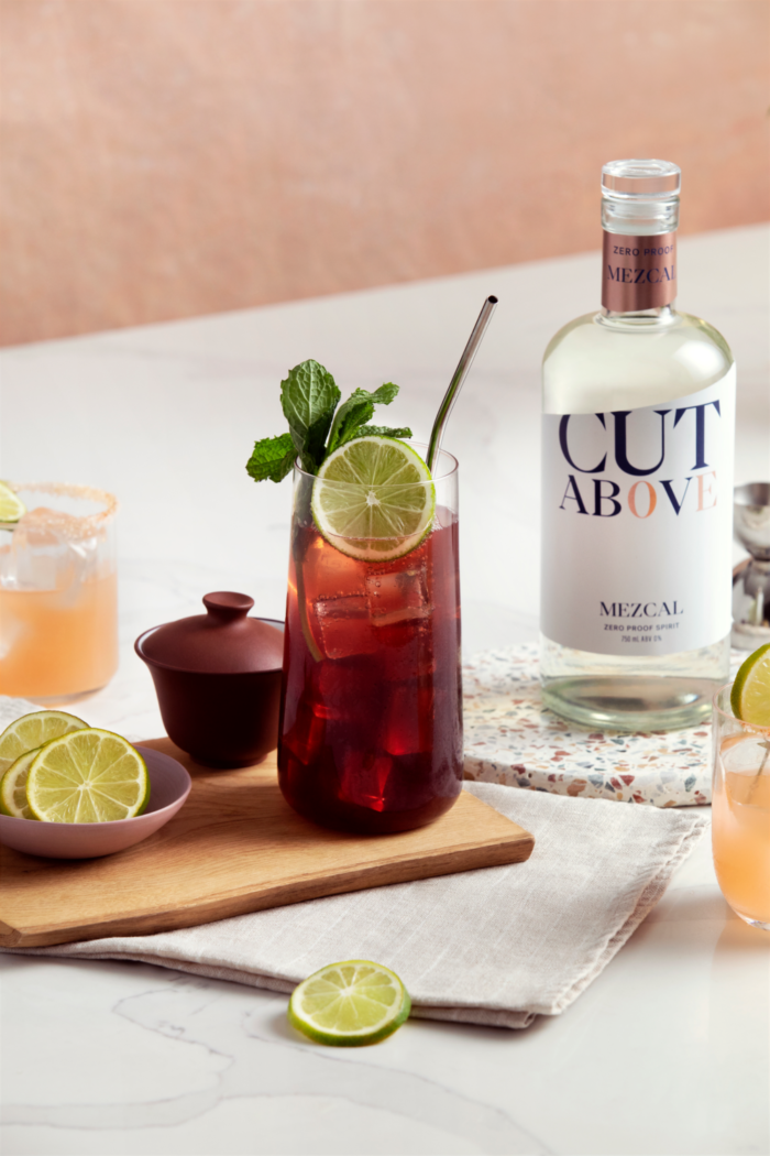 Cut Above Mezcal bottle showcased with refreshing cocktails garnished with lime and mint in a vibrant setting.